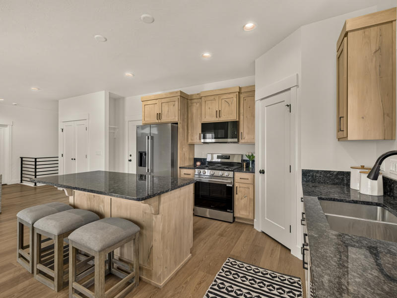 Kitchen with light wood cabinets, stainless appliances, and a dark stone island